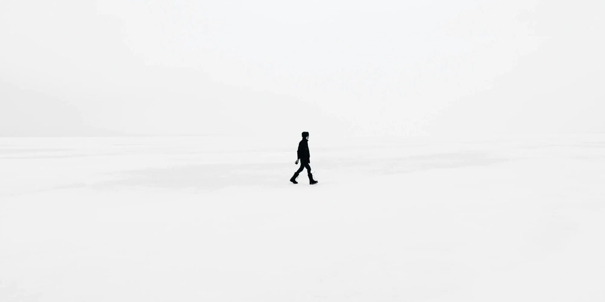 A lone figure in black crossing a white field of snow