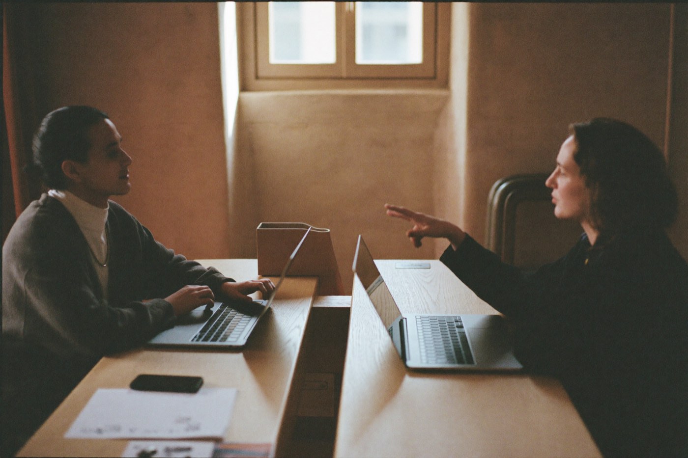 Two people talking across a pale oak meeting table