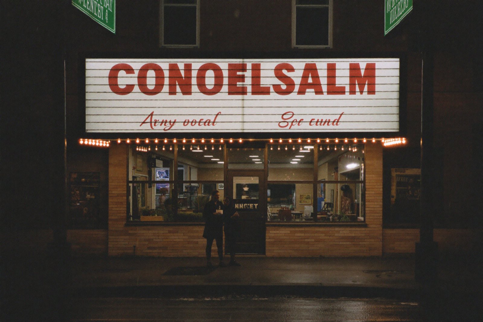 A neighborhood cinema marquee glowing over a rain-wet street