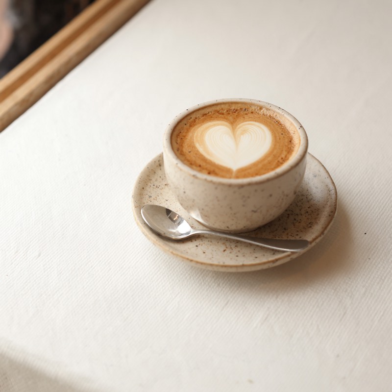 A cappuccino with heart latte art and a spoon on the saucer