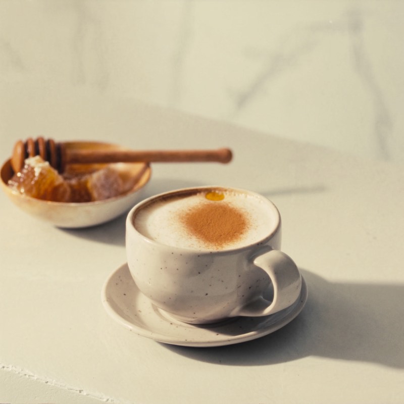A cinnamon-dusted honey latte with a honey dipper on the saucer