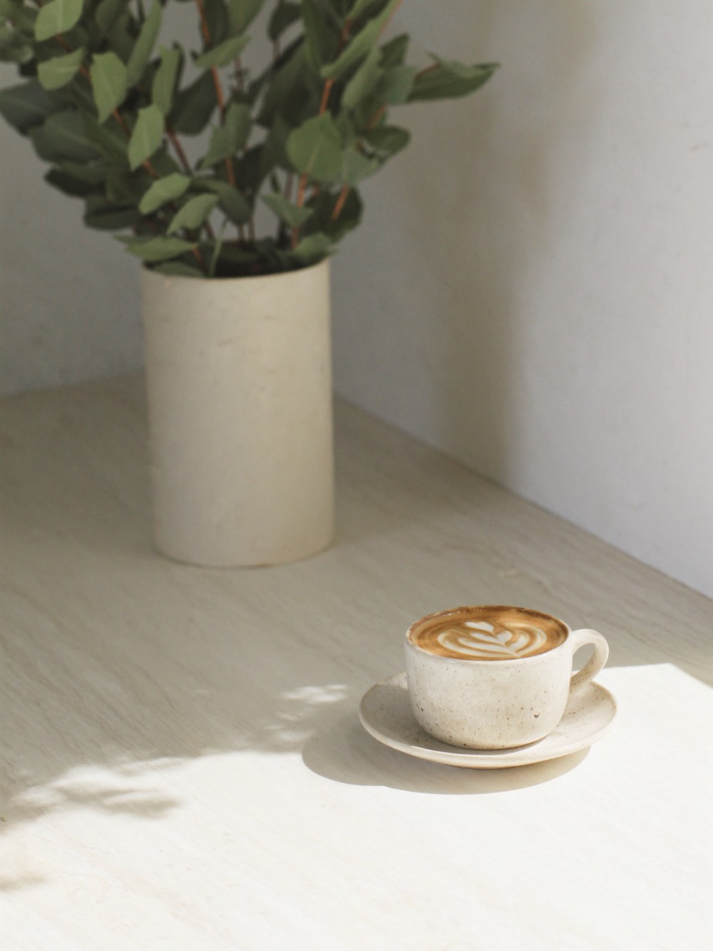 A cappuccino with rosetta latte art beside a vase of eucalyptus