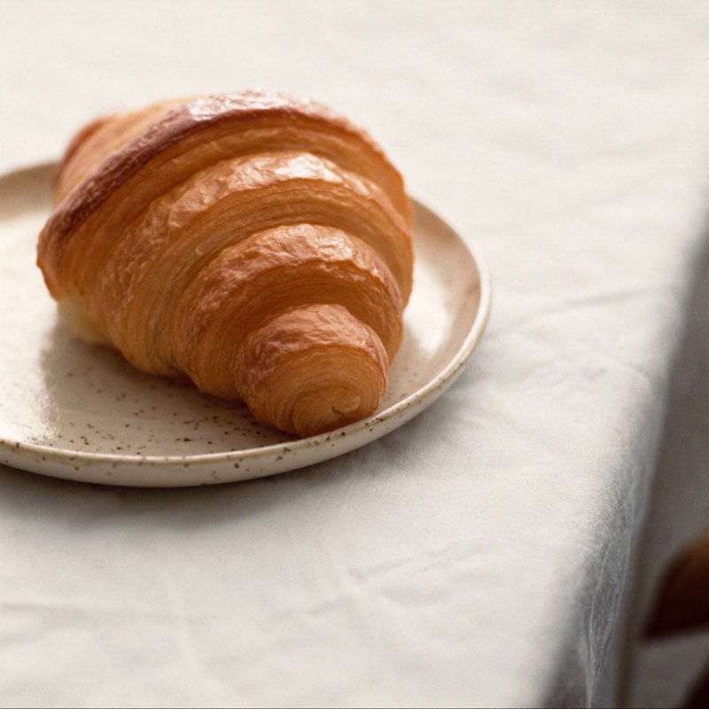 A golden butter croissant with crisp flaky layers on a ceramic plate