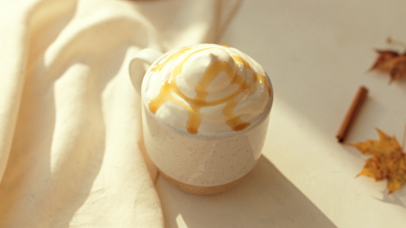 A maple latte topped with whipped cream beside autumn leaves